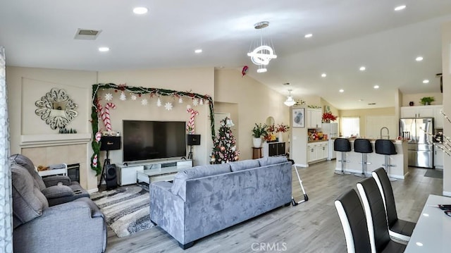 living room with a chandelier, light hardwood / wood-style floors, and vaulted ceiling