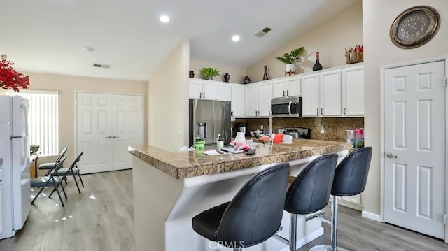 kitchen featuring a kitchen breakfast bar, white cabinets, stainless steel appliances, and light hardwood / wood-style floors