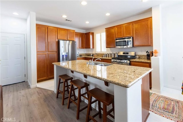 kitchen with a center island with sink, a kitchen breakfast bar, sink, appliances with stainless steel finishes, and light hardwood / wood-style floors