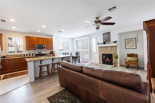 living room with ceiling fan, a healthy amount of sunlight, light hardwood / wood-style floors, and a fireplace