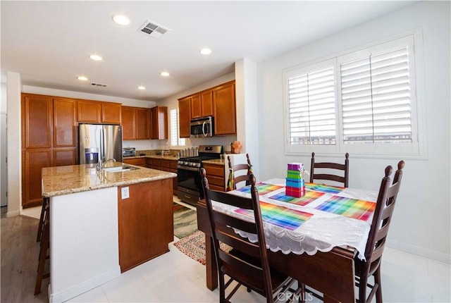 kitchen with light stone countertops, appliances with stainless steel finishes, a breakfast bar, sink, and a center island with sink