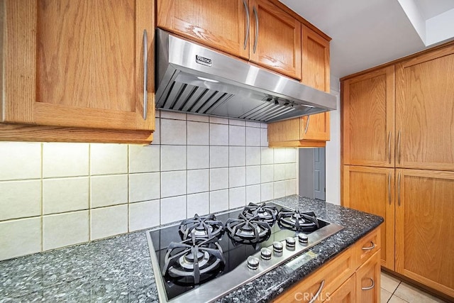 kitchen featuring ventilation hood, dark stone counters, stainless steel gas stovetop, decorative backsplash, and light tile patterned floors