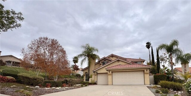 view of front of house with driveway, an attached garage, a chimney, stucco siding, and a tiled roof