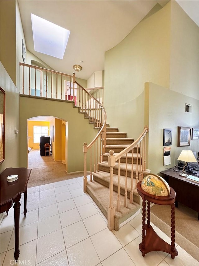 staircase featuring tile patterned flooring, a skylight, arched walkways, and a towering ceiling