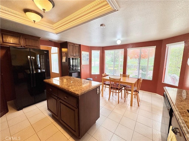 kitchen featuring a center island, crown molding, a tray ceiling, light tile patterned floors, and black appliances