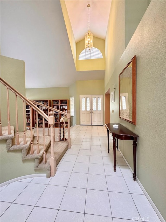 tiled entrance foyer with stairs, a notable chandelier, baseboards, and high vaulted ceiling