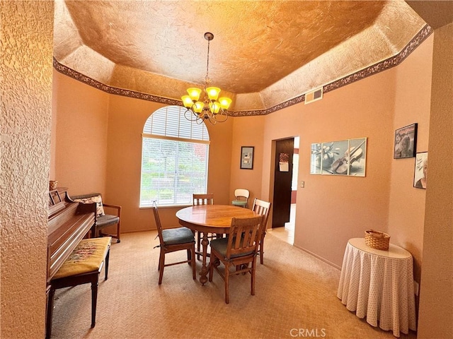 dining area featuring light carpet, visible vents, an inviting chandelier, and a tray ceiling