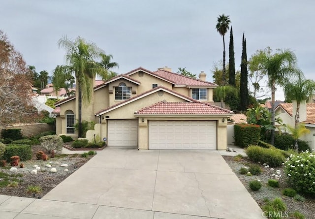 mediterranean / spanish house featuring driveway, a chimney, stucco siding, a garage, and a tiled roof