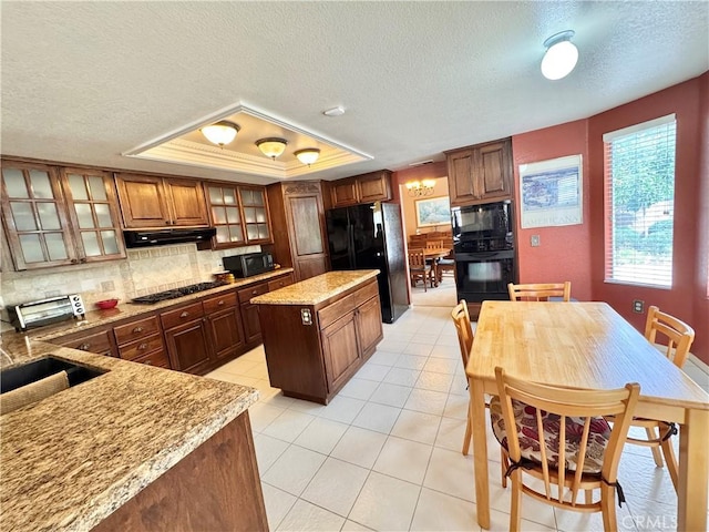 kitchen featuring extractor fan, a tray ceiling, light stone counters, decorative backsplash, and black appliances