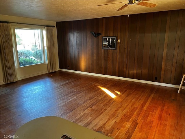 spare room with hardwood / wood-style flooring, ceiling fan, a textured ceiling, and wood walls