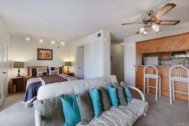 bedroom featuring ceiling fan, white refrigerator, track lighting, a textured ceiling, and light carpet