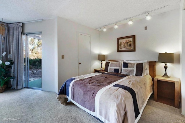 carpeted bedroom with access to outside, track lighting, and a textured ceiling