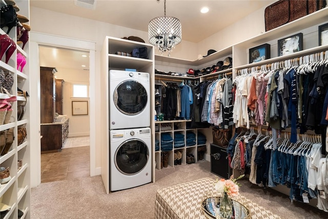 laundry room featuring tile patterned flooring, stacked washer / drying machine, and an inviting chandelier