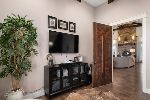 living room with beam ceiling, dark hardwood / wood-style flooring, and a stone fireplace