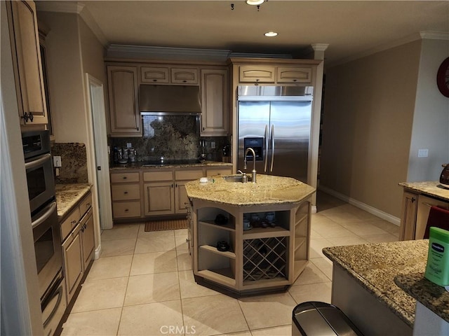 kitchen featuring black electric stovetop, backsplash, sink, a center island with sink, and built in fridge