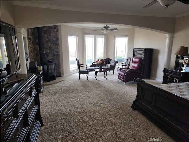 bedroom featuring carpet flooring, decorative columns, ornamental molding, access to outside, and a wood stove