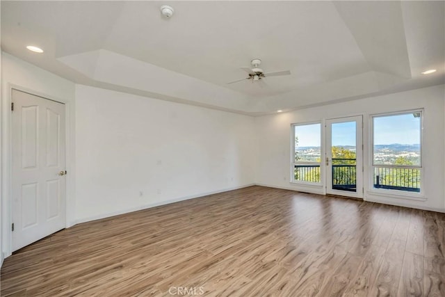 spare room with light hardwood / wood-style floors, a raised ceiling, and ceiling fan