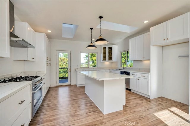 kitchen with a skylight, stainless steel range, wall chimney exhaust hood, white cabinets, and light wood-type flooring