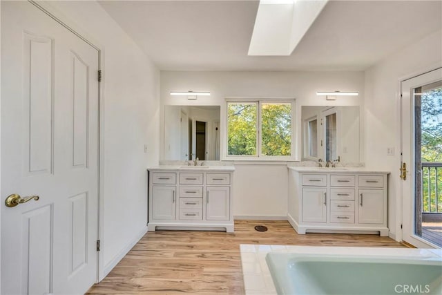 bathroom featuring wood-type flooring, vanity, a skylight, and a healthy amount of sunlight