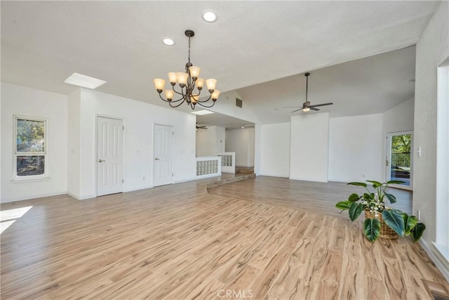 unfurnished living room with ceiling fan with notable chandelier, light hardwood / wood-style flooring, and vaulted ceiling