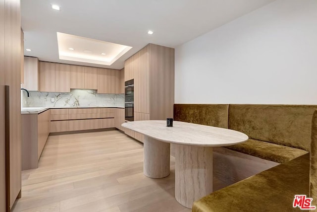 kitchen with sink, light hardwood / wood-style flooring, tasteful backsplash, light brown cabinetry, and a tray ceiling