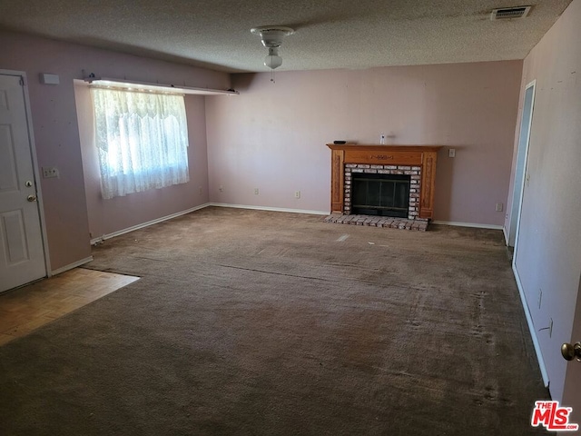 unfurnished living room with dark colored carpet, a textured ceiling, a brick fireplace, and ceiling fan