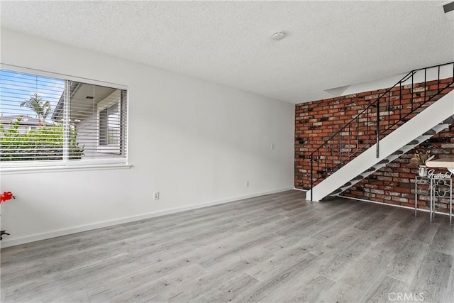 unfurnished room with brick wall, a textured ceiling, and hardwood / wood-style flooring