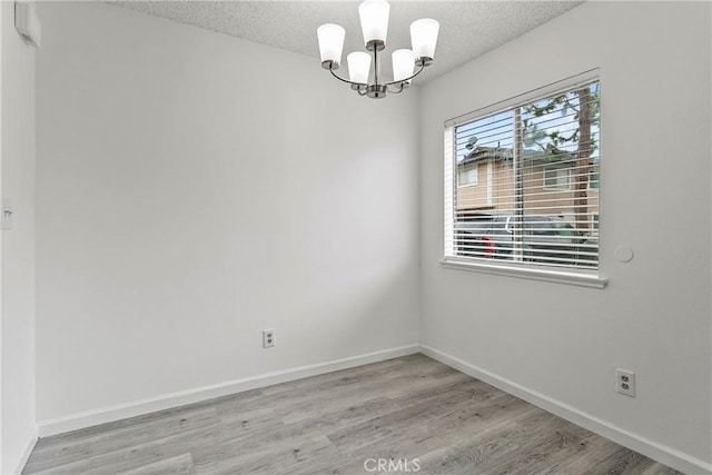 unfurnished room with light hardwood / wood-style floors, a textured ceiling, and a notable chandelier