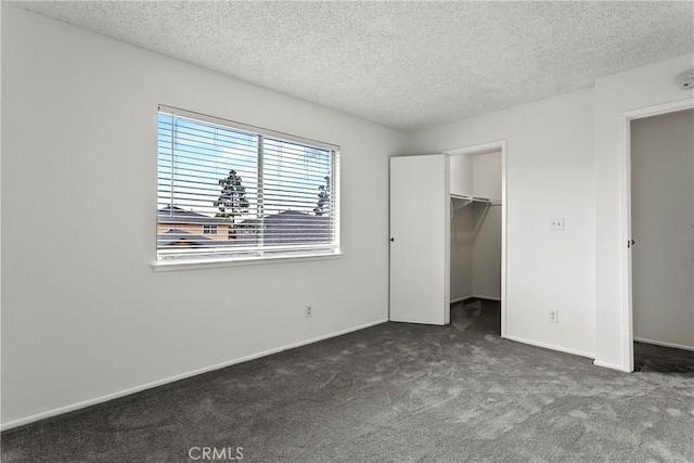 unfurnished bedroom featuring dark carpet, a spacious closet, a textured ceiling, and a closet