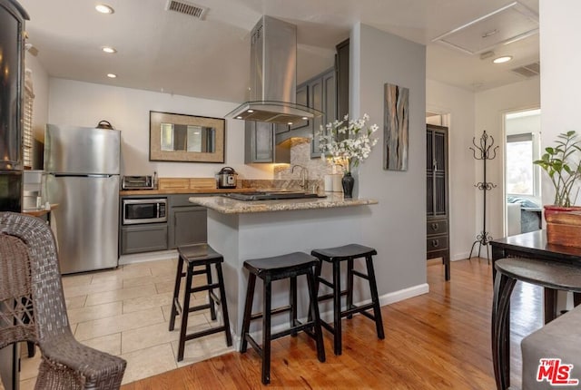 kitchen with island exhaust hood, appliances with stainless steel finishes, light wood-type flooring, kitchen peninsula, and gray cabinetry