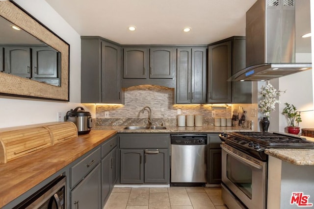 kitchen featuring wooden counters, appliances with stainless steel finishes, backsplash, wall chimney exhaust hood, and sink