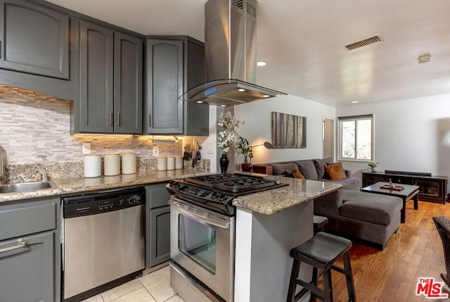 kitchen featuring sink, light stone counters, light hardwood / wood-style floors, extractor fan, and appliances with stainless steel finishes