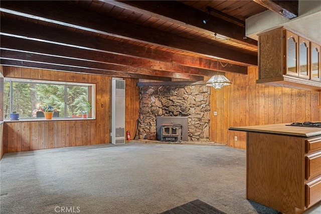 unfurnished living room featuring a wood stove, wooden ceiling, beamed ceiling, wood walls, and carpet