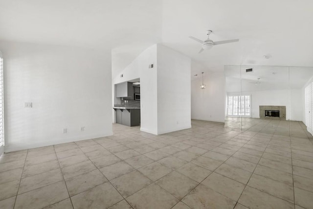 unfurnished living room with ceiling fan, a tile fireplace, and lofted ceiling