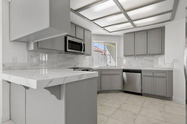 kitchen featuring a kitchen breakfast bar, stainless steel appliances, gray cabinetry, and kitchen peninsula