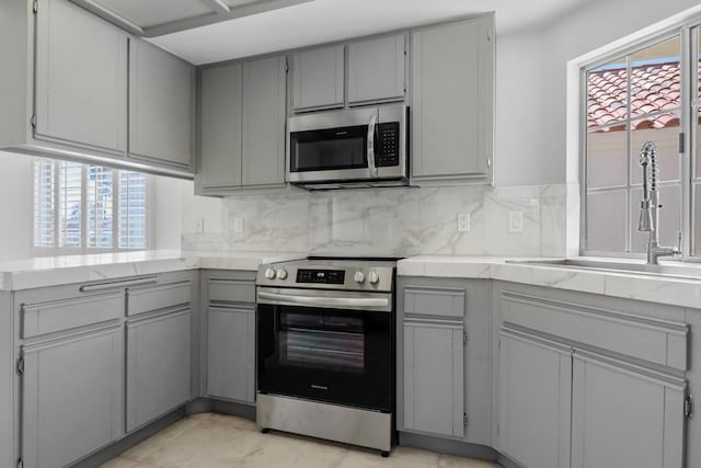 kitchen with sink, backsplash, gray cabinets, and stainless steel appliances