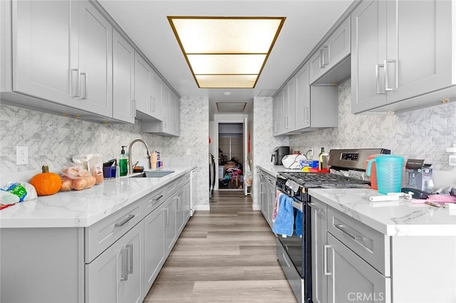 kitchen with gray cabinets, light wood-type flooring, stainless steel range with gas cooktop, and sink