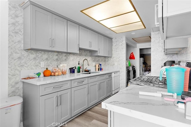 kitchen featuring gray cabinetry, dishwasher, sink, light hardwood / wood-style flooring, and washer and clothes dryer