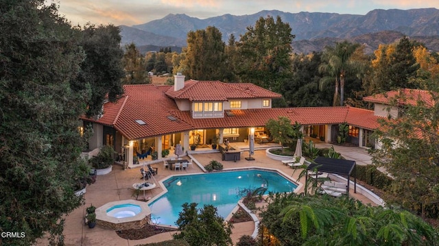 pool at dusk featuring an in ground hot tub, a mountain view, and a patio