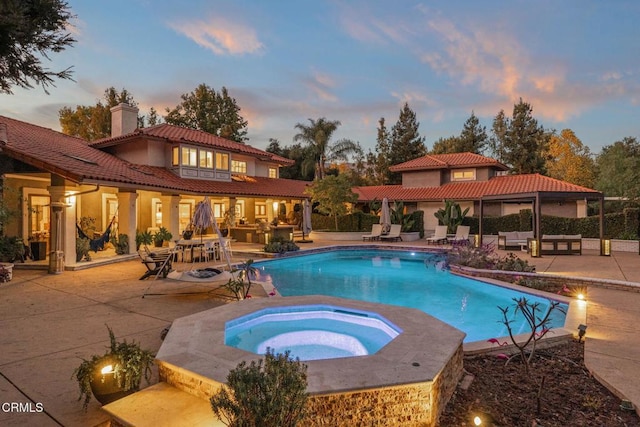 pool at dusk featuring outdoor lounge area, an in ground hot tub, and a patio