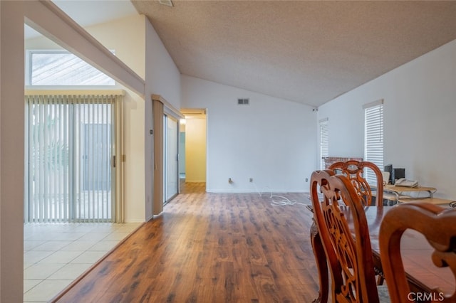 dining area with hardwood / wood-style flooring, a textured ceiling, and vaulted ceiling