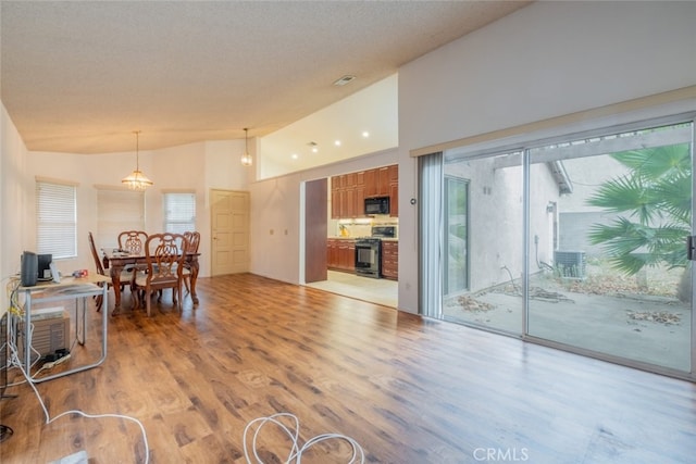 interior space with vaulted ceiling, black appliances, an inviting chandelier, light hardwood / wood-style flooring, and hanging light fixtures