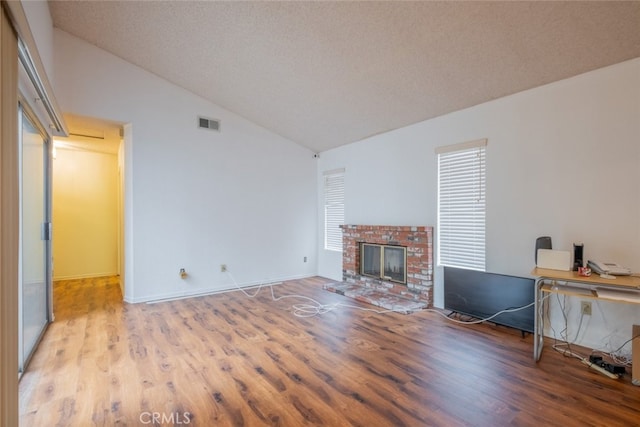 unfurnished living room featuring a textured ceiling, hardwood / wood-style flooring, a brick fireplace, and high vaulted ceiling