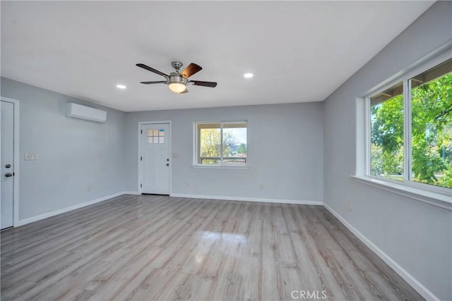 spare room featuring a wall unit AC, ceiling fan, a wealth of natural light, and light hardwood / wood-style floors