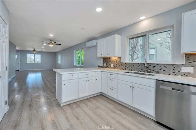 kitchen featuring a wall mounted AC, stainless steel dishwasher, kitchen peninsula, sink, and white cabinets