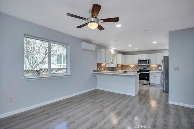 kitchen with an AC wall unit, kitchen peninsula, white cabinetry, light hardwood / wood-style flooring, and stainless steel appliances