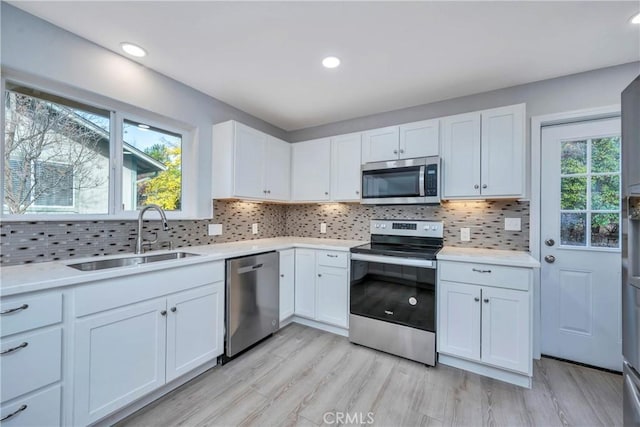 kitchen featuring appliances with stainless steel finishes, backsplash, white cabinets, light hardwood / wood-style flooring, and sink