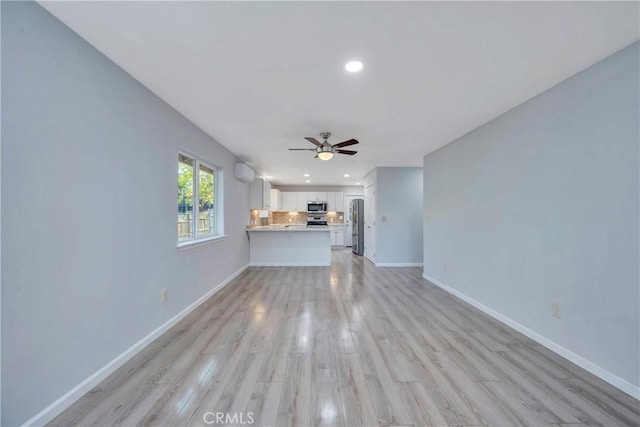 unfurnished living room with ceiling fan, a wall unit AC, and light wood-type flooring