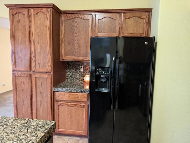 kitchen with decorative backsplash, black refrigerator with ice dispenser, dark stone countertops, and light tile patterned floors