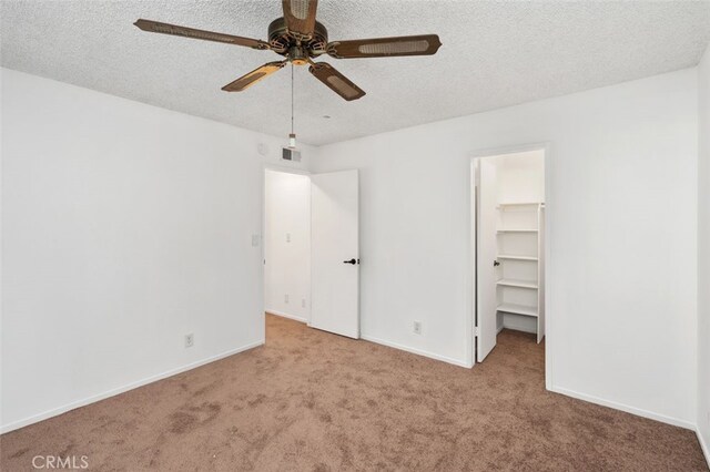 unfurnished bedroom with a spacious closet, a closet, ceiling fan, and light colored carpet